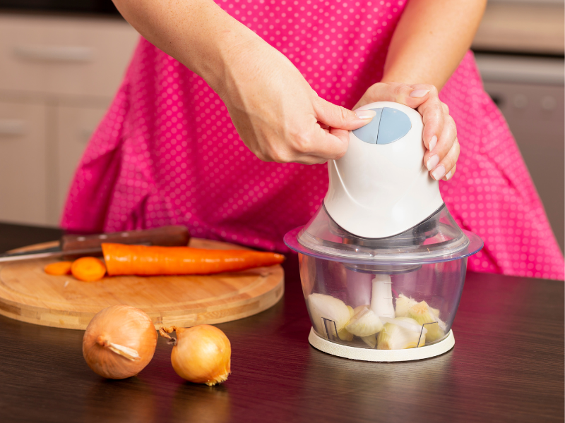 Woman in a pink dress chopping garlic with food chopper at a kitchen island