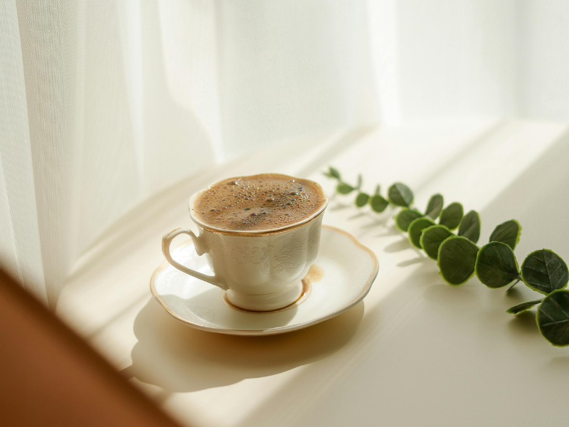 a cup of coffee in an antique looking mug and sauces sitting in the sunlight on a table