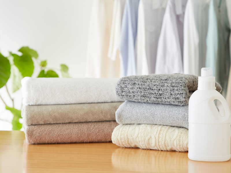 a photo of neatly folded laundry, detergent, and a plant in the background