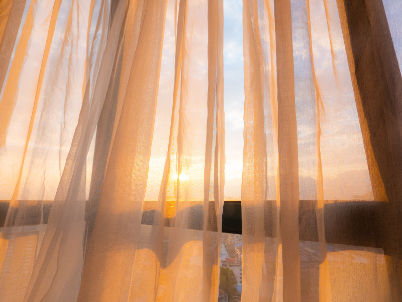 a photo of sheer curtains and morning light streaming through