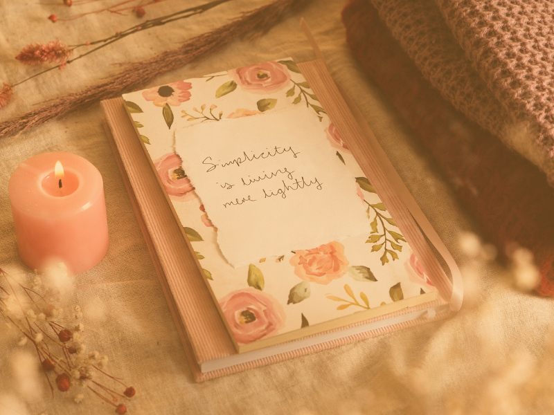 a pink journal with flowers that says simplicity is living more lightly and a pink candle