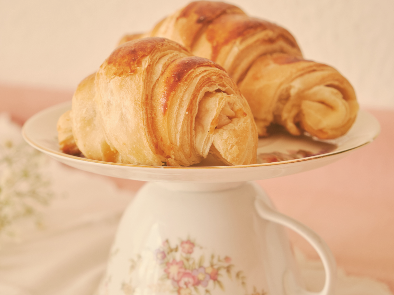 a white and pink floral tea cup cake stand holding two croissants
