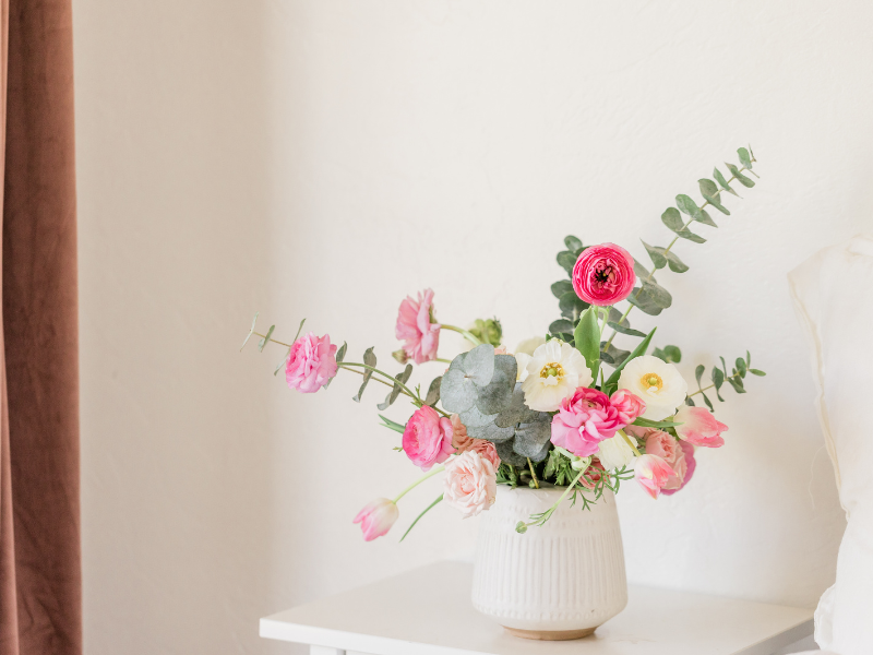 a white vase on table with pink and white flowers and eucalyptus