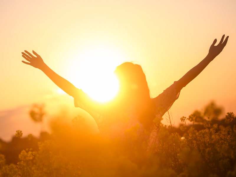 a woman with arms up outside while sun is rising