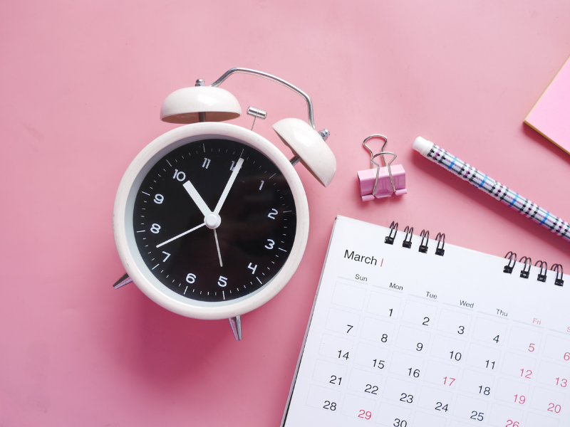 photo of alarm clock with calendar on a pink background