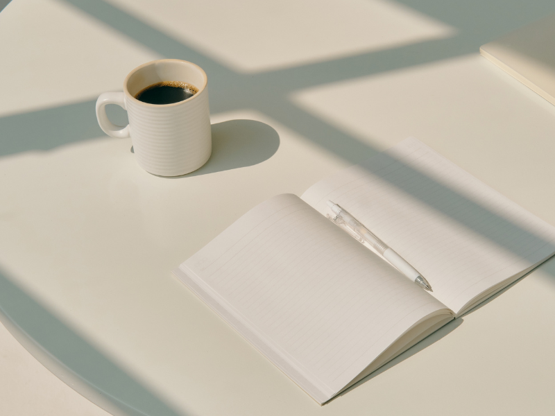 white table with a blank notebook and cup of black coffee