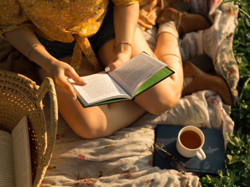woman sitting on picnic blanket outside in the sun reading