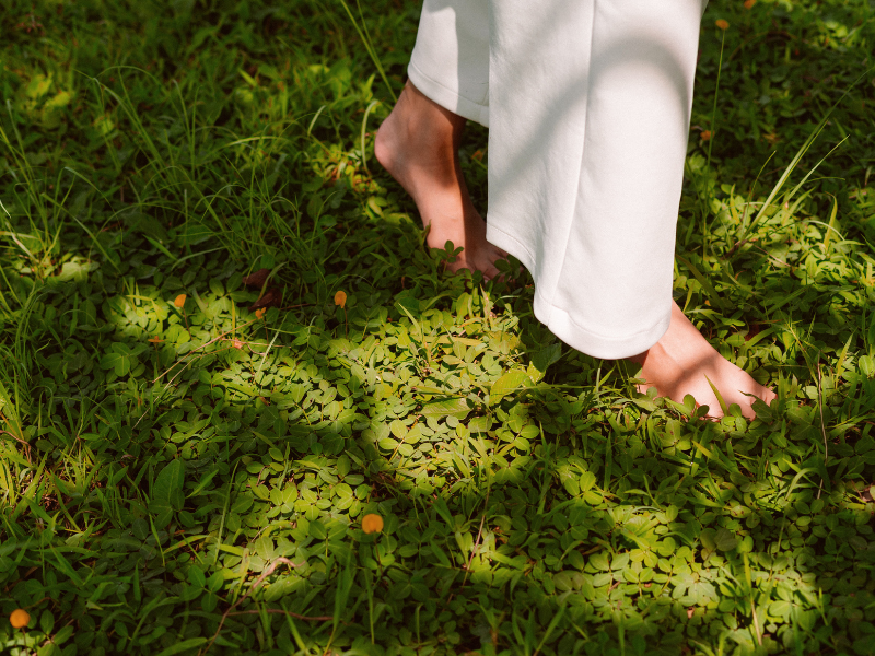 woman stepping on shaded grass outside barefoot with white pants